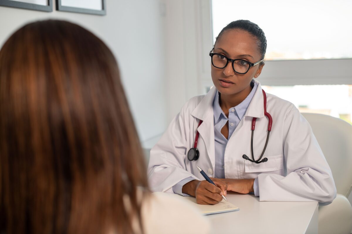 Doctor wearing glasses listening to female patient.