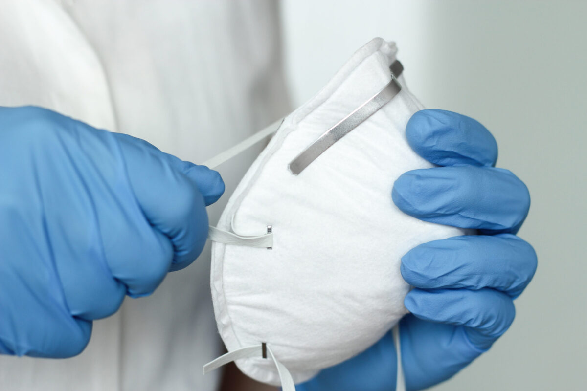 Hands with blue protective nitride gloves holding N95 respirator.