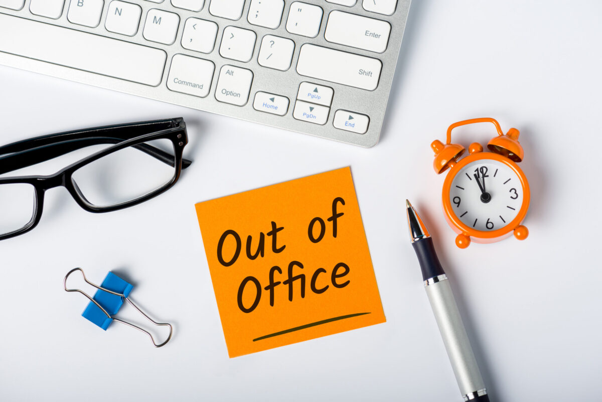 Out of office - memo on office desk with glasses, pen, clock, paperclip.