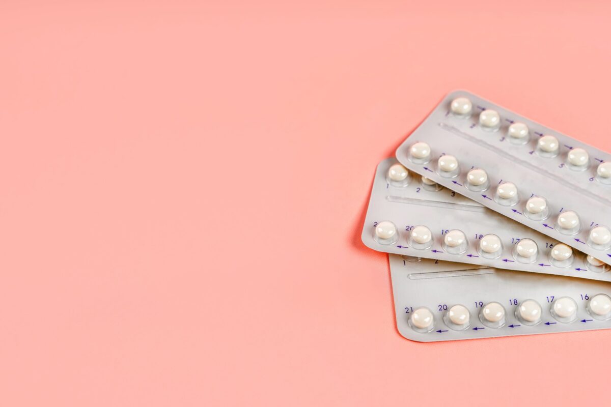 Three blister packs of birth control pills on a pink background.