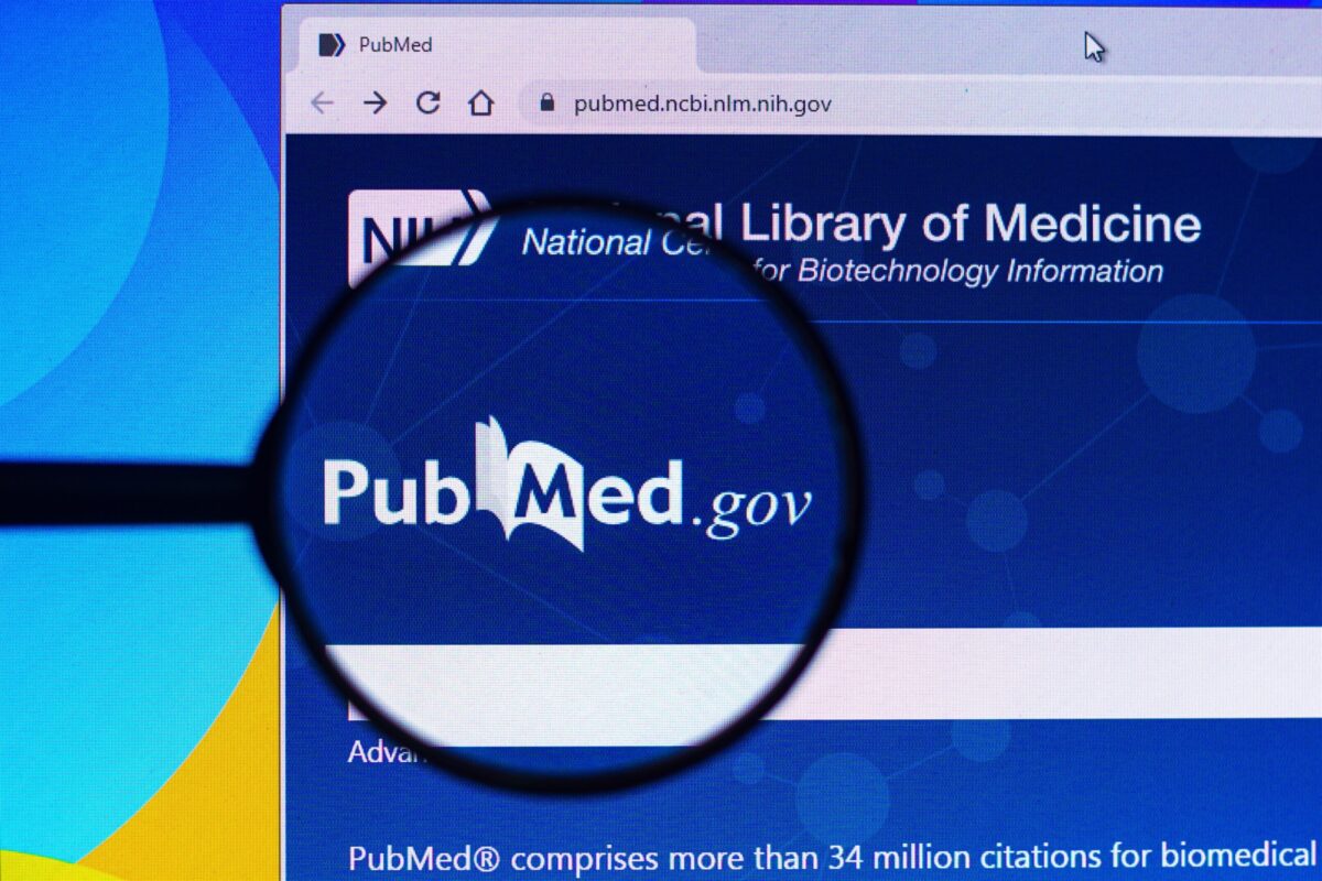 the homepage of the PubMed website is seen on a computer screen through a magnifying glass.