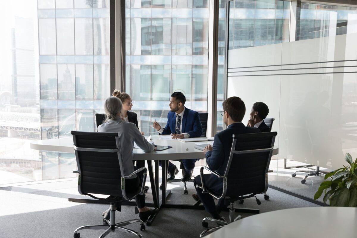 five multi ethnic business people negotiating in modern boardroom.