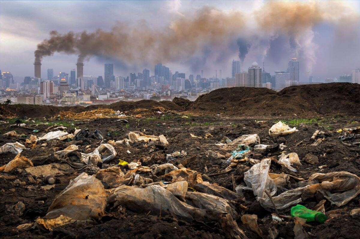 City with trash in foreground and smokestacks producing smog in background.