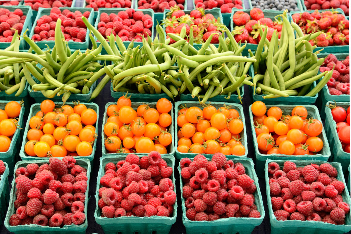 Berries, tomatoes, and green beans in small green containers at farmer's market.